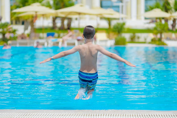 Naklejka premium Boy spending time in pool at resort. He is jumping eagerly in to the swimming pool and enjoying his summer holidays.