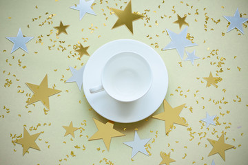 Obraz na płótnie Canvas White cup and saucer on a yellow background with sparkles stars