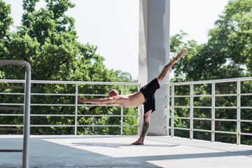 Young male with tattoos do yoga exercises outdoors on balcony	