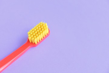 Red plastic toothbrush with bright yellow bristles with selective focus on blurred purple background with empty space for text. Toothbrush for daily cleaning of teeth and caries protection 