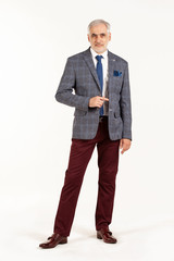 Portrait of smart and handsome intelligent senior man in stylish grey jacket and dark red pants isolated on white background
