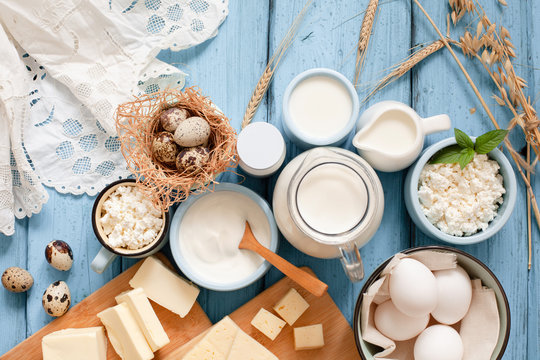 Different types of dairy products on blue wooden background: milk, sour cream, cottage cheese, cheese, cream, yogurt, eggs and butter top view with copy space
