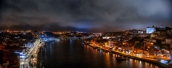 Panoramic landscape of night cloudy Porto, Portugal with city lights, Douro river and boats