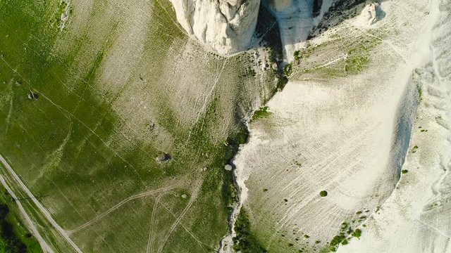 Top view of relief of surface of cliff. Shot. Dizzying top view of white cliff on background of green foot. Reliefs of surface of earth with rocky mountains