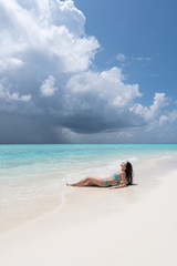 Fototapeta na wymiar A young girl in a turquoise swimsuit is lying on a white beach.
