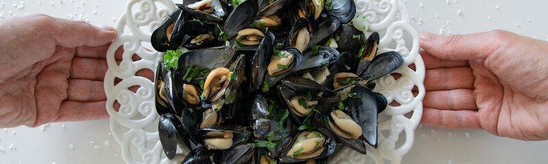 Top view of woman hands holding a plate with cooked delicious black mussel. Healthy eating concept, rich protein  food