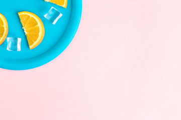 Flat lay of plastic plate with orange fruit slices and ice cubes against pastel pink background minimal creative concept. Space for copy.