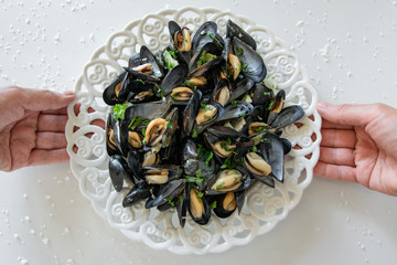 Top view of woman hands holding a plate with cooked delicious black mussel. Healthy eating concept, rich protein  food