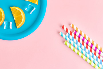 Orangeade abstract made of colorful drinking straws and orange fruit slices with ce cubes on plate...