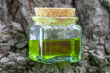 Glass bottle with cork cap with green-yellow nectar oil. Located on the bark of coniferous wood
