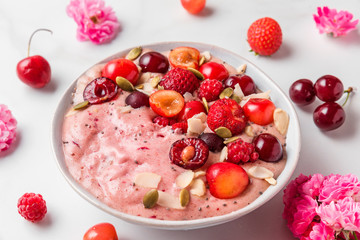 pink smoothie bowl or nice cream with fresh berries, rose flowers, nuts and seeds on white marble table