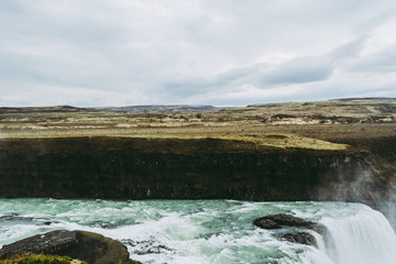 Horizontal view of Gullfoss waterfall in Southwest Iceland. Blue and green water with pale white splashes flying over it. Icelandic landscapes.