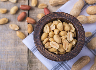 Peanuts in small dark wooden bowl on natural rustic desk.