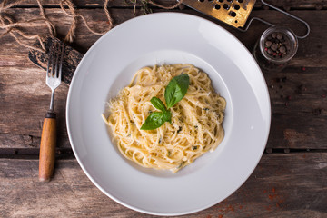 Delicious creamy Italian spaghetti pasta starter with cheese and fresh basil on rustic wooden table