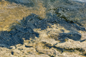 Natural liquid texture. River wave runs on the rocky shore.