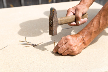 Old hammer and nail in the hands of an elder man. Carpenter hammers a nail into a tree. Old hammer and nail in the hands of an elder man. Carpenter hammers a nail into a tree.