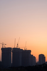 Industrial construction cranes and building silhouette against the sunset sky .