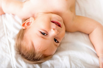 Fototapeta na wymiar Happy baby toddler laying on the white bedding and smiling. Top view. Happy child