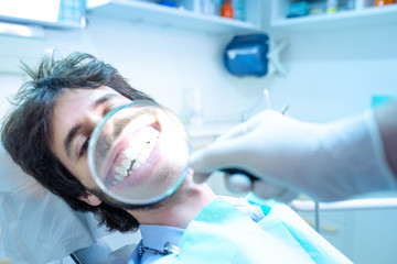 Giovane ragazzo seduto sulla poltrona del dentista, fa vedere il suo stupendo sorriso con la lente...