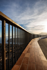 Obraz premium Metallic and wooden railing on a coast cliff illuminated by the sunset light