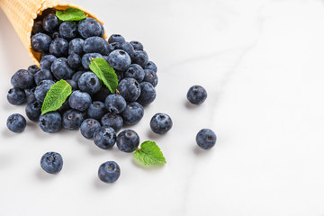 blueberries with mint in waffle ice cream cone on white marble background. summer food concept