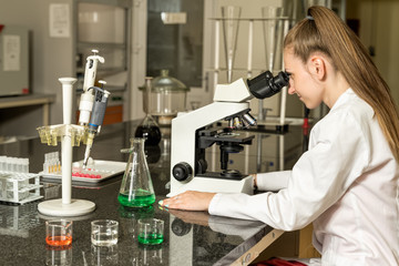 Young female laboratory technician working on compound microscope