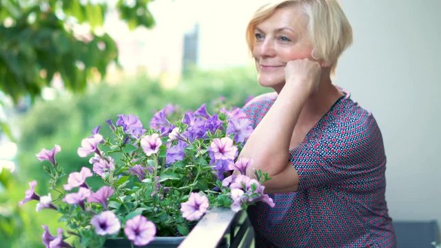 Portrait of beautiful, senior woman enjoying flowers on the balcony, 4K