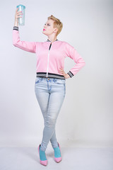 pretty plus size short hair woman with blue cup of water. blonde adult girl wearing sport pink jacket and jeans posing on white studio background alone.