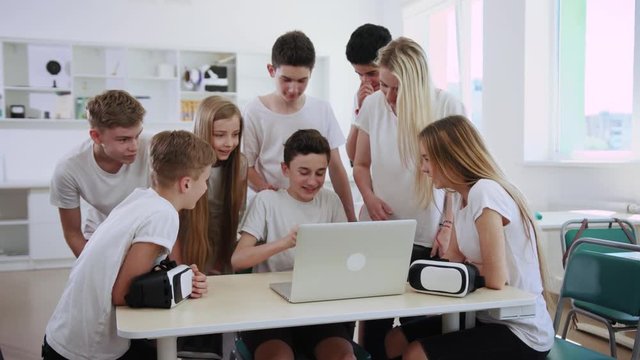 Group of excited teen students trying new gadgets wearing VR headset during a break in a tech class.