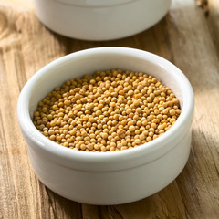 Yellow mustard seeds in small bowl, photographed on wood with natural light (Selective Focus, Focus one third into the seeds)