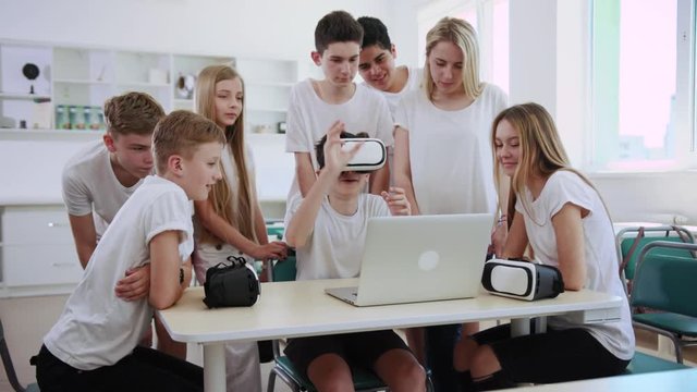 Nice fun education process. Group of excited students experiencing virtual reality trying VR headset during a break in classroom.