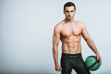 Muscle male model in black treand sportswear posing with a basket ball on gray background. Studio shoot.
