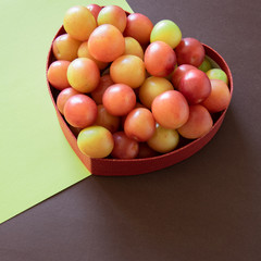 Organic fresh plums in heart shape box   on geometric background. Healthy vegetarian food. Still life with space for text