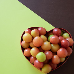 Fototapeta na wymiar Organic fresh plums in heart shape box on geometric background. Healthy vegetarian food. Still life with space for text.