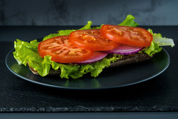 Breakfast tomato sandwich with salad on black stone background.