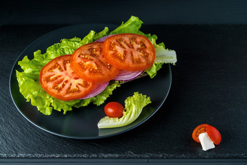 Breakfast tomato sandwich with salad on black stone background.