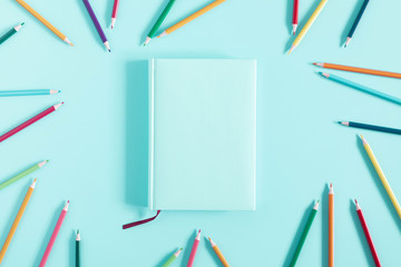 Color pencils and notebook on blue background. Back to school background. Flat lay, top view, copy space