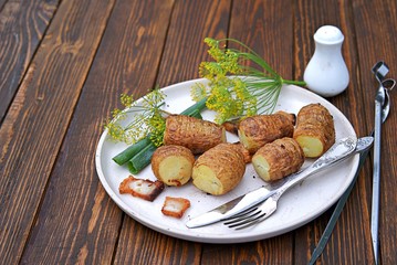 Grilled potatoes with bacon, baked whole on skewers, on a white clay plate on a wooden background. Potato harvest. Selective focus