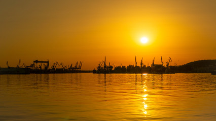 Beautiful sunset in the sea port. Orange sky with magically reflecting sun on the waves of the sea, Gdynia, Poland.