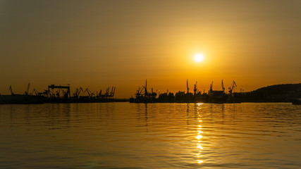 Beautiful sunset in the sea port. Orange sky with magically reflecting sun on the waves of the sea,...