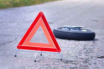 Red emergency triangle stop sign on the road. Spare wheel and wheel wrench on a backdrop.