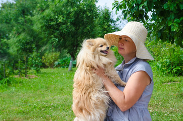 young woman in a hat holds on hands a white German Pomeranian Spitz in the garden.