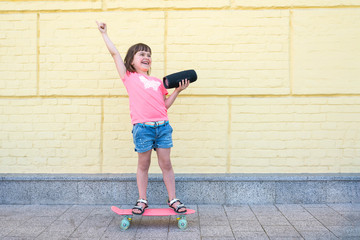 A cute child of 6-7 years rides a skateboard with a musical bluetooth column outdoors. Idea....