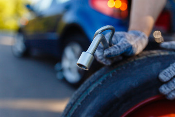 Close-up of a man's hand with spare wheel and cylinder key on the background of the car on the Jack. Mechanic wearing gloves with a spare wheel of a car with a flat wheel. Replacing tires on the road