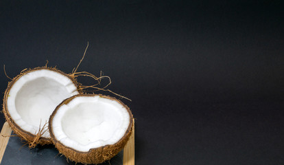 Coconut exotic fruit, two coconut halves in the shell, black background, on the kitchen and blackboard with wood and stone, selective focus