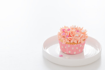 Cupcake decorated with pink cream on a white plate on a white background. Place for text.