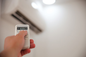The woman switching on air conditioner while sitting in armchair at home
