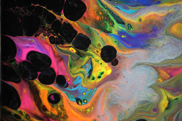 Abstract acrylic pour painting in black with vibrant neon colors dancing through resembling flames.