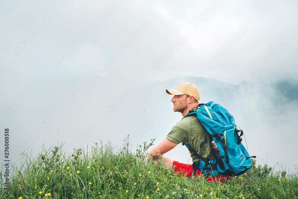 Wall mural tired hiker with backpack man resting and enjoying cloudy valley bottom walking by the foggy cloudy 