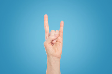 Hand show rock gesture on a blue background, close up.
